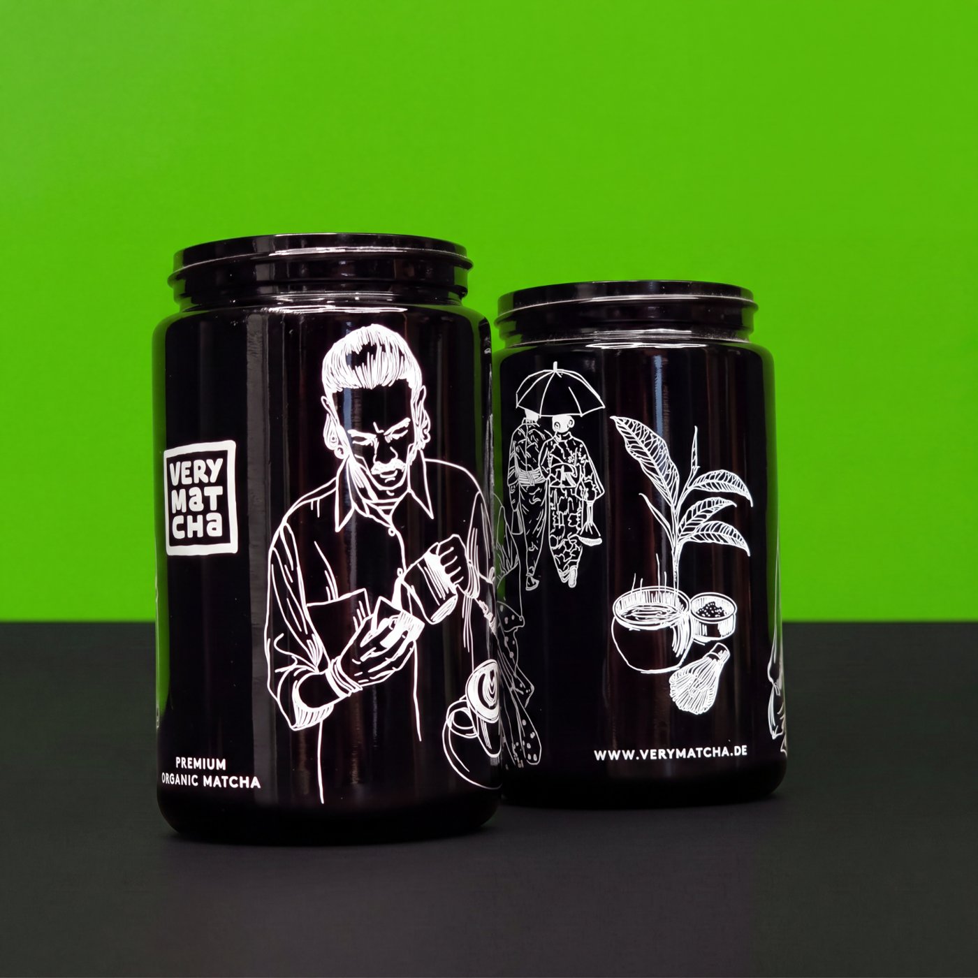Zwei schwarze Glasdosen mit weißem, illustrativem Siebdruck